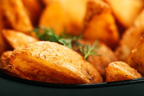 close up view of delicious golden potato wedges with dill in bowl