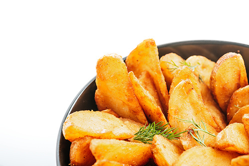 close up view of delicious golden potato wedges with dill in bowl isolated on white