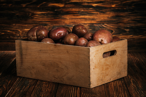 fresh ripe potatoes in box on wooden background