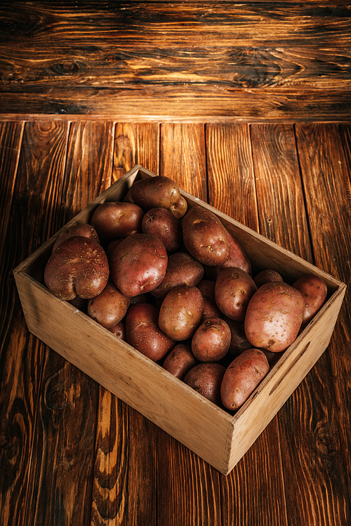 fresh ripe potatoes in box on wooden background