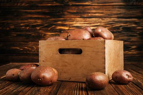 fresh ripe potatoes in box and around on wooden background