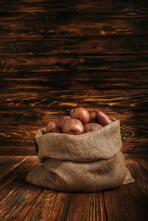 ripe potatoes in rustic sack on wooden background