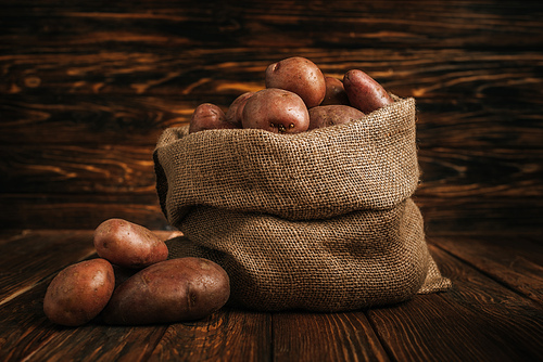 ripe potatoes in rustic sack on wooden background