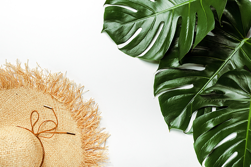 top view of green palm leaves, straw hat on white background