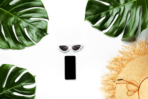 top view of green palm leaves, straw hat, sunglasses and notepad with smartphone on white background