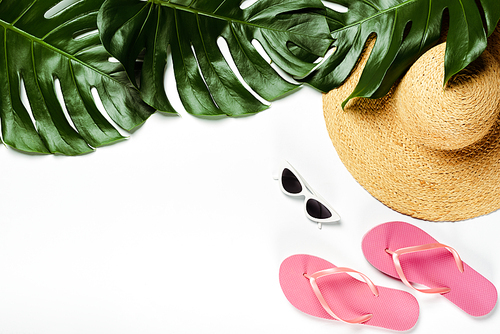 top view of green palm leaves, straw hat, sunglasses and flip flops on white background