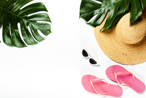 top view of green palm leaves, straw hat, sunglasses and flip flops on white background