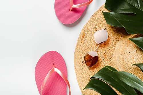 top view of green palm leaves, straw hat, sunglasses and flip flops on white background