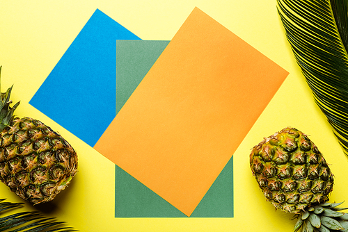 top view of green palm leaves and ripe pineapples on colorful background