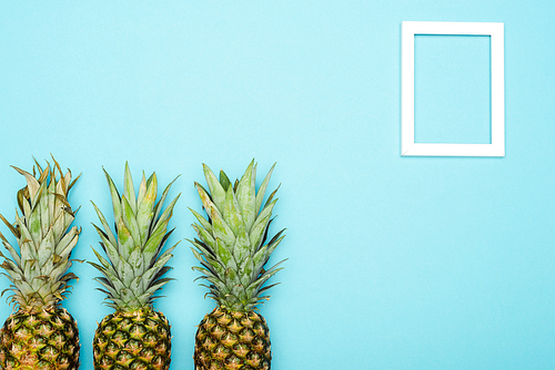 top view of ripe pineapples near square empty frame on blue background