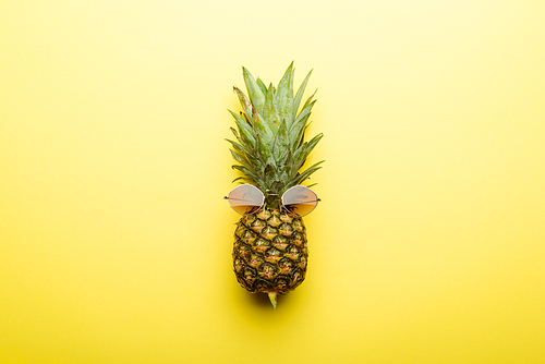 top view of ripe pineapple in sunglasses on yellow background