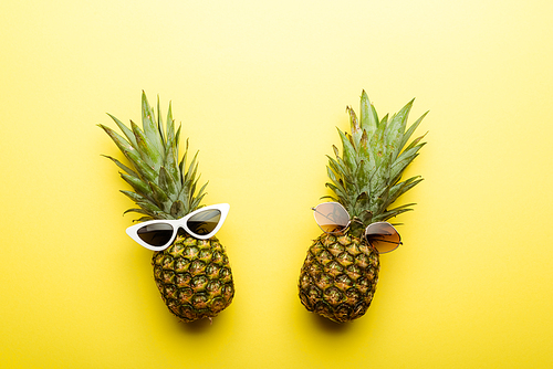 top view of ripe pineapples in sunglasses on yellow background