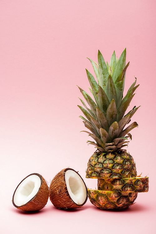 cut ripe pineapple and fresh coconut halves on pink background