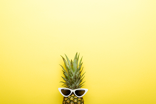 top view of ripe pineapple in sunglasses on yellow background