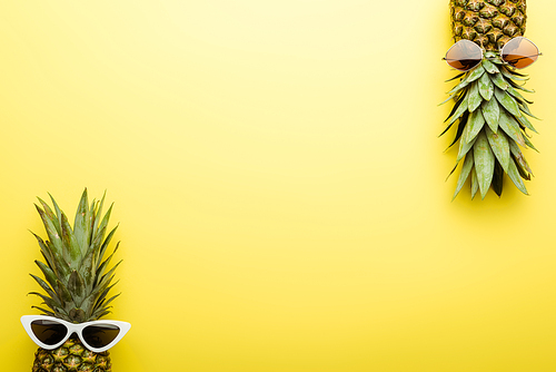 top view of ripe pineapples in sunglasses on yellow background