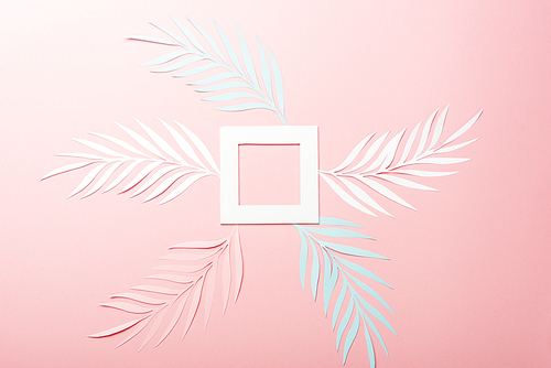 top view of white, pink and blue paper cut palm leaves and square frame on pink background