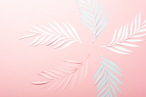 top view of white, pink and blue paper cut palm leaves on pink background