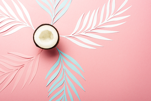 top view of white, pink and blue paper cut palm leaves and coconut half on pink background