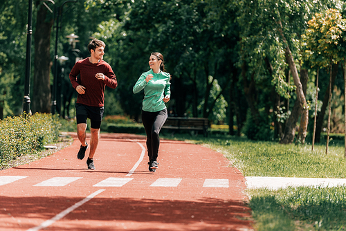 Couple smiling at each other while jogging on running track in park