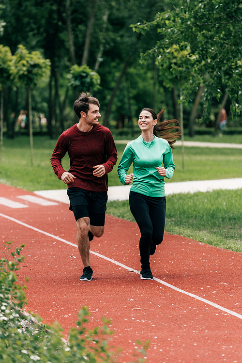 Selective focus of sportswoman smiling at boyfriend while jogging in park