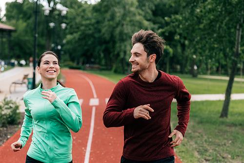 Smiling man looking at positive girlfriend while jogging in park