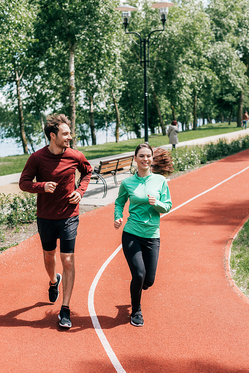 Handsome man smiling near girlfriend during jogging in park