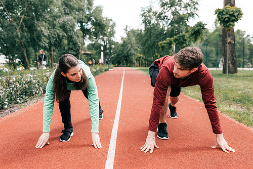 Couple looking at each other while standing in starting position on running track in park