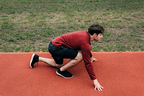 Side view of sportsman in starting position on running track while working out in park