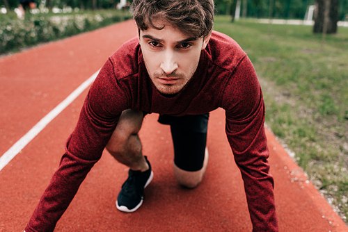 Handsome man standing in starting position on running track in park