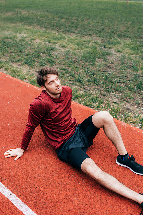 Exhausted sportsman sitting on running path in park