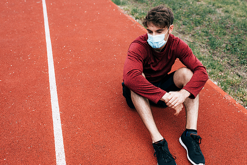 Sportsman in medical mask sitting on running track in park