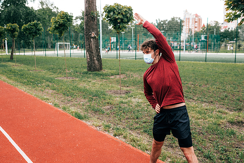 Sportsman in medical mask exercising on track in park