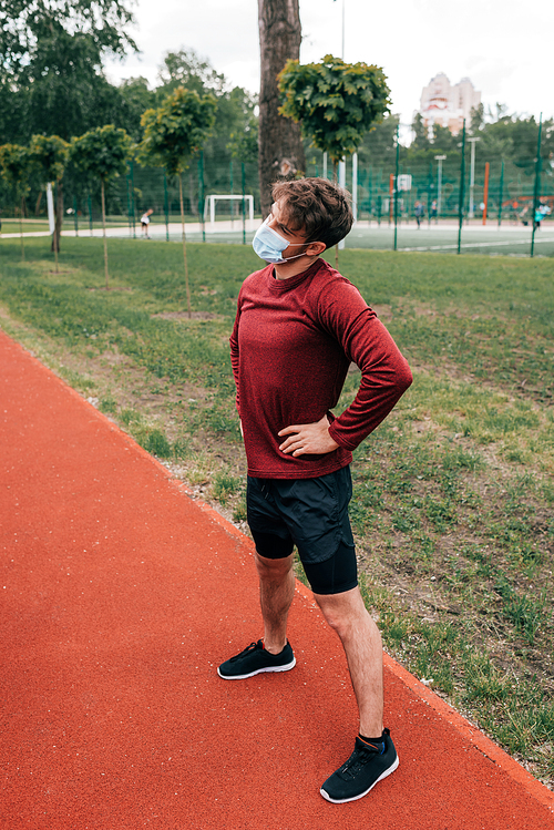 Sportsman in medical mask with hands on hips training in park
