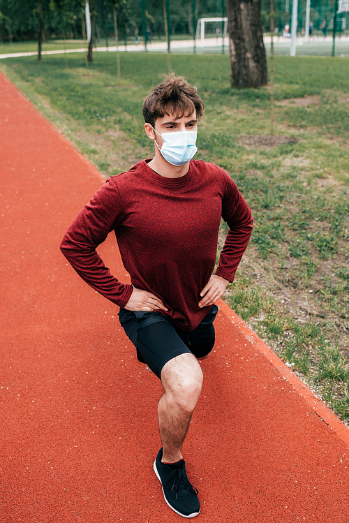Sportsman in medical mask doing lunges on running track in park