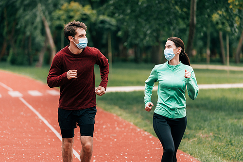 Young couple in medical masks jogging on running track in park