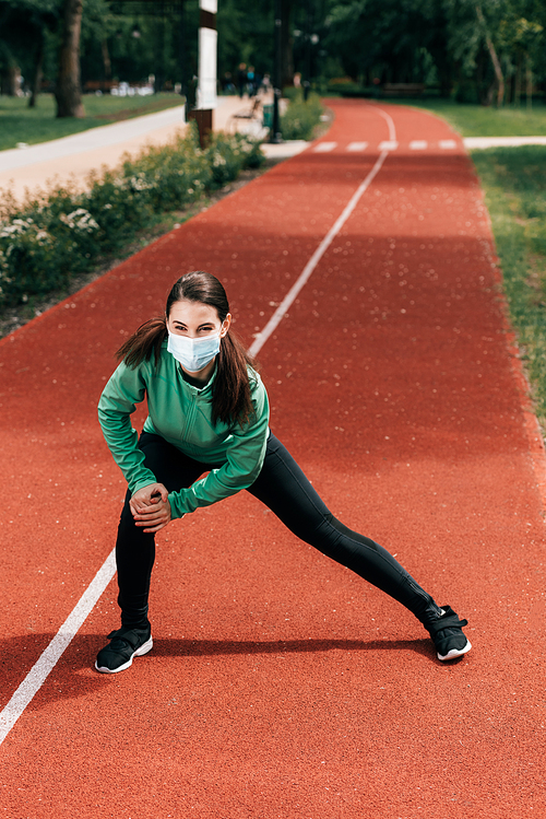 Sportswoman in medical mask working out on running track in park