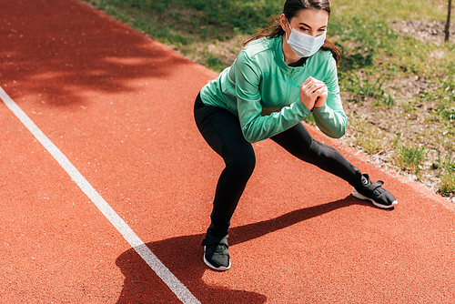 Sportswoman in medical mask doing lunges on track in park