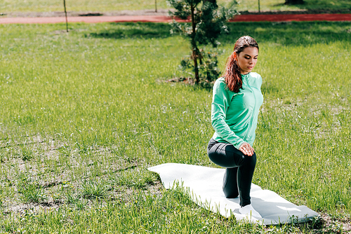 Sportswoman exercising on fitness mat on grass in park