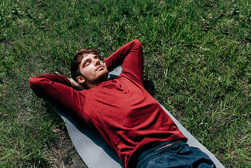 High angle view of handsome sportsman lying on fitness mat in park