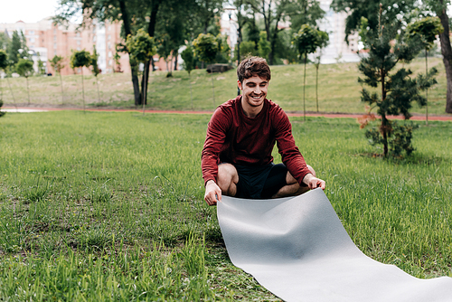 Handsome man smiling while laying fitness mat on grass in park