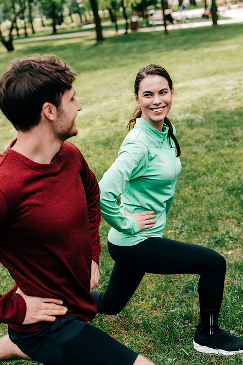 Selective focus of beautiful woman smiling at man while doing lunges in park