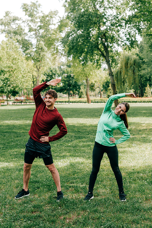Young smiling couple working out on grassy lawn in park