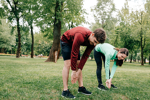 Young couple smiling while stretching together in park