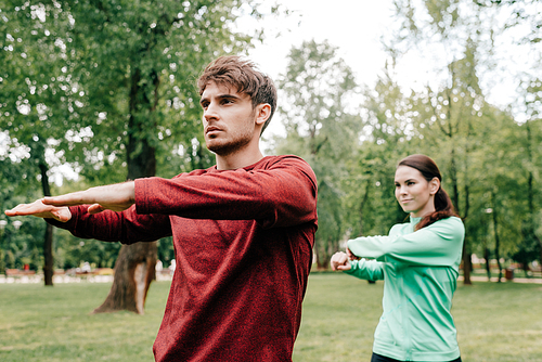Selective focus of sportsman warming out near girlfriend in park