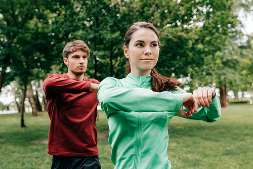 Selective focus of attractive woman warming out with boyfriend during training in park