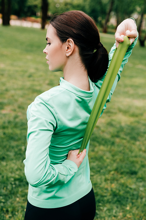 Back view of young sportswoman using resistance band while exercising in park