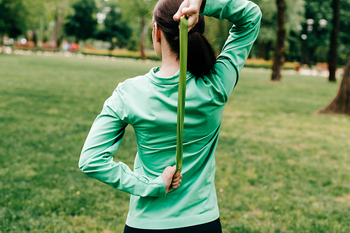 Back view of sportswoman pulling up resistance band in park