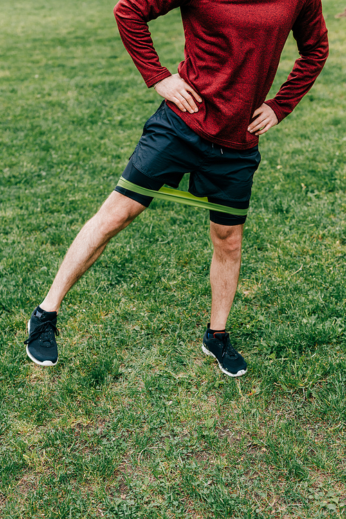 Cropped view of sportsman with hands on hips exercising with elastics band in park