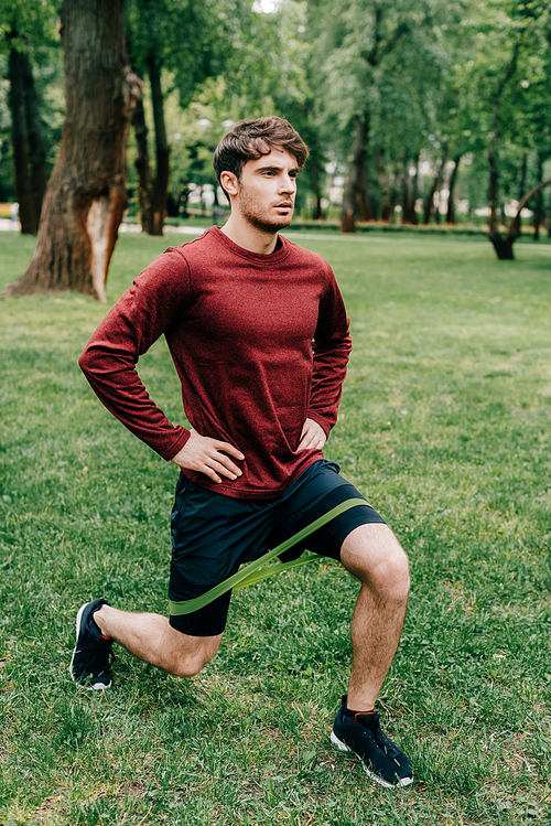 Handsome sportsman doing lunges while training with resistance band in park