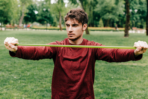 Handsome sportsman pulling up elastics band in park